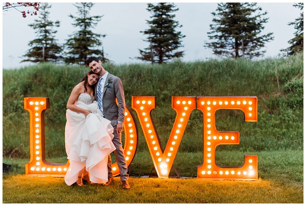 Bride lays head on groom's chest in front of LOVE marquee sign| tree-farm wedding| Belcroft Estate Wedding| Toronto wedding photographer| Ontario wedding photographer| 3photography