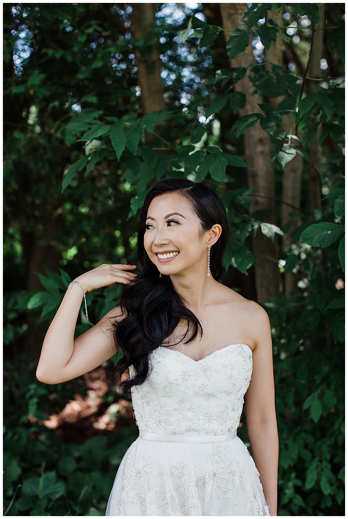 Bride smiling and looking to the side while sweeping hair over her shoulder| outdoor bridal portrait| Bride under tree| asian bride| sweetheart neckline gown| Toronto photographer| 3photography