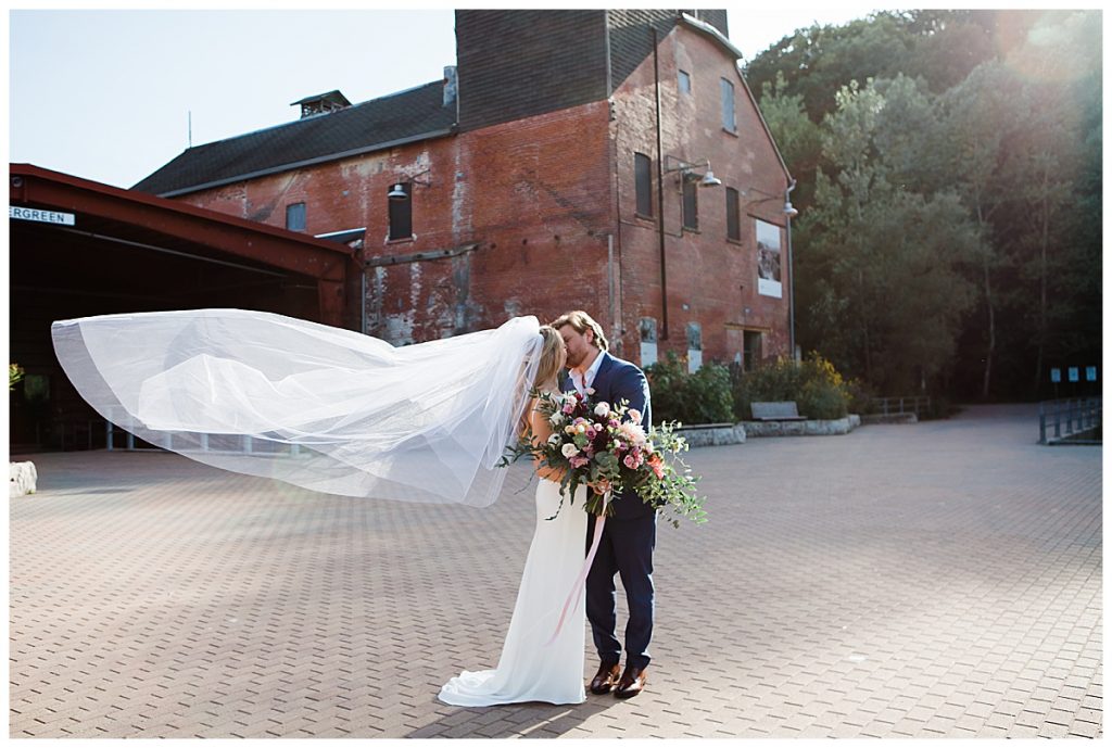 Bride and groom kiss while wedding veil flows in wind