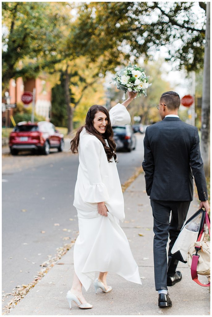 Bride and groom walk down street while bride looks over shoulder| Toronto wedding photographer| 3photography